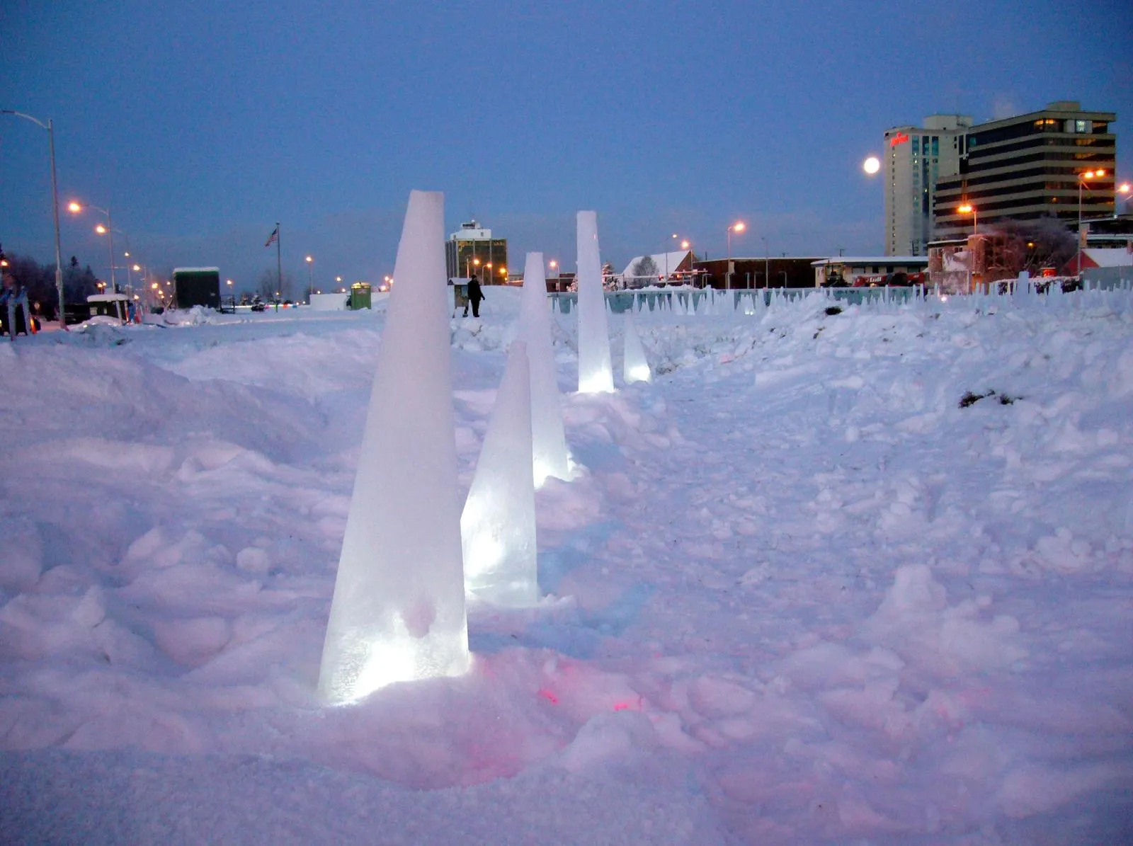 Lit pylon casts embedded in ice across Delaney Park at dusk